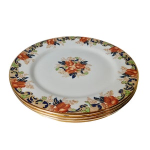 May include: A set of four white ceramic dinner plates with a gold rim and a floral design in shades of blue, orange, and green.