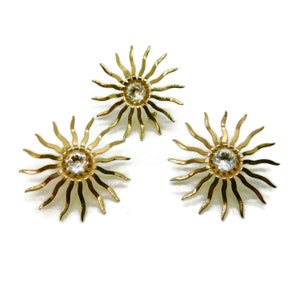 May include: Three gold sun-shaped brooches with clear rhinestone centers.