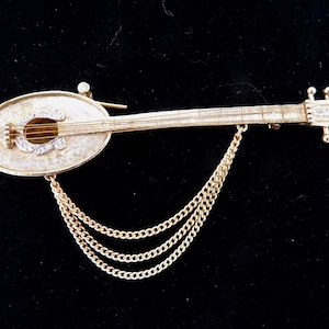 May include: A gold-tone brooch in the shape of a guitar with a chain attached. The guitar is decorated with rhinestones.