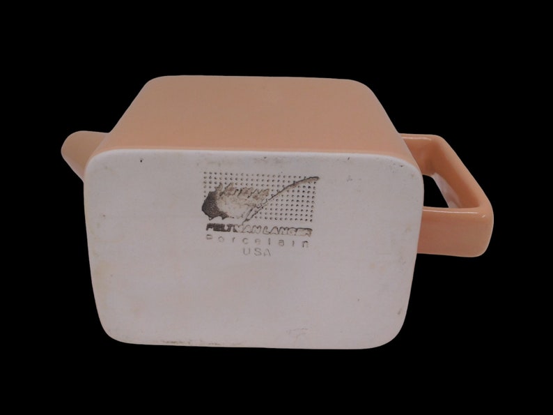 Peut inclure: Une th&eacute;i&egrave;re en c&eacute;ramique de couleur p&ecirc;che avec un corps carr&eacute; et une poign&eacute;e. Le fond de la th&eacute;i&egrave;re porte une &eacute;tiquette blanche avec le texte "Fitz and Floyd Porcelain USA".