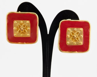 May include: A pair of red square-shaped earrings with gold accents. The earrings feature a gold design with a four-leaf clover motif.