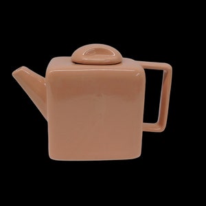 Peut inclure: Une th&eacute;i&egrave;re carr&eacute;e avec un couvercle et une poign&eacute;e. La th&eacute;i&egrave;re est en c&eacute;ramique et de couleur rose clair.