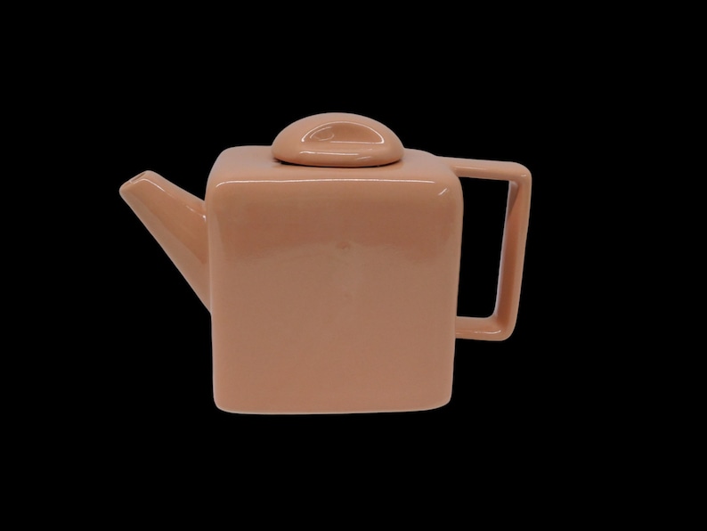 Peut inclure: Une th&eacute;i&egrave;re carr&eacute;e avec un couvercle et une poign&eacute;e. La th&eacute;i&egrave;re est en c&eacute;ramique et de couleur rose clair.