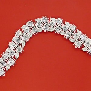 May include: A silver bracelet with a floral design. The bracelet is made of small, white flowers and leaves. The bracelet is on a red background.