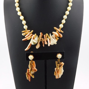 May include: A vintage jewelry set featuring a necklace and matching earrings. The necklace has a strand of cream-colored beads with gold-tone accents and a coral-like pendant. The earrings have a similar design, with cream-colored beads and coral-like accents.