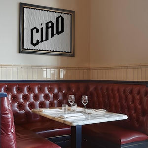 May include: A red leather booth with a white marble table and two wine glasses. The booth is in a corner of a room with white tile walls and a framed black and white mosaic with the word "CIAO" on it.