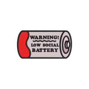 Puede incluir: Parche bordado con forma de pila, con un extremo curvo rojo y un borde gris y negro. El texto "WARNING! LOW SOCIAL BATTERY" está bordado en negro sobre un fondo gris claro.