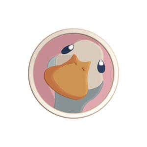 Könnte beinhalten: Gestickter Aufnäher mit dem Gesicht einer Cartoon-Ente. Die Ente hat einen großen orangefarbenen Schnabel, blaue Augen und einen hellblauen Hals. Der Aufnäher ist kreisförmig, mit einem rosa Hintergrund und einem cremefarbenen Rand.