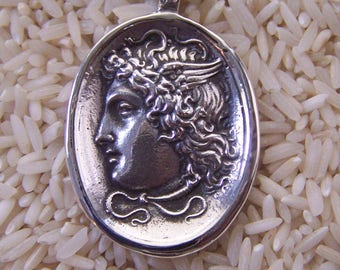 May include: Silver pendant necklace featuring a detailed profile of a woman with a laurel wreath. The pendant is oval shaped and has a textured surface.