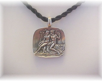 May include: Silver pendant necklace with a detailed relief sculpture of a couple embracing. The pendant is square shaped and has a black cord.