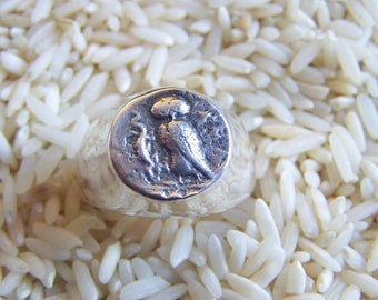 May include: A silver ring with an owl design on the face. The ring is set against a background of white rice.