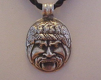 May include: Silver pendant necklace featuring a detailed face with a crown of leaves and a protruding tongue. The pendant is attached to a black cord.