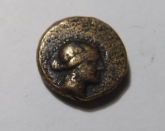 May include: A circular bronze-toned coin featuring a raised relief profile of a figure wearing a helmet. The surface of the coin has a weathered, textured appearance with dark patina accents highlighting the details of the embossed portrait.