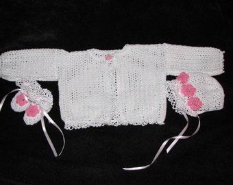 May include: A white crocheted baby sweater set with pink flower accents. The set includes a cardigan, a bonnet, and booties.