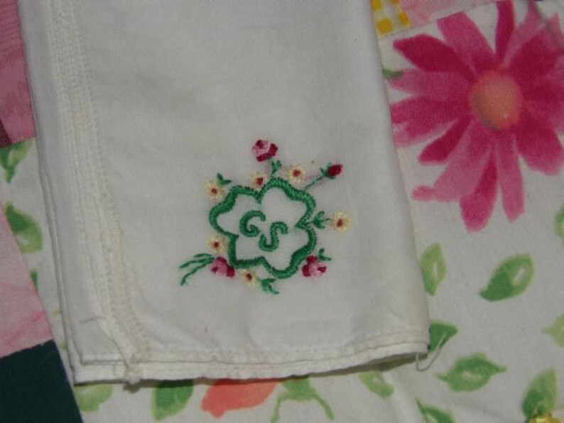 May include: White handkerchief with green embroidered clover and the letters "GS" in the center. The clover is surrounded by small pink and yellow flowers.