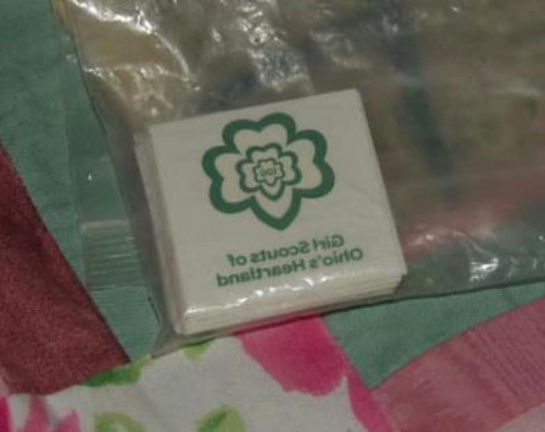 May include: A white package of Girl Scout cookie patches with a green four-leaf clover logo. The text on the package reads "Ohio's Heartland Girl Scouts of".
