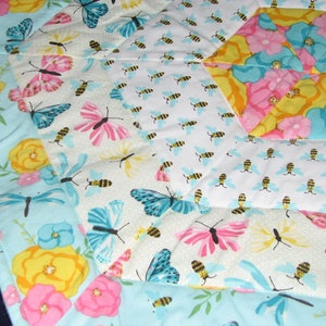 Pode incluir: Uma colcha de retalhos com um padrão hexagonal que apresenta uma variedade de desenhos florais e de borboletas. A colcha é feita com um tecido azul claro, branco, amarelo, rosa e turquesa.