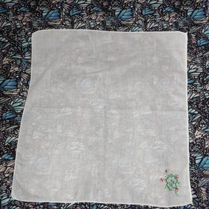 May include: A white cotton handkerchief with a small embroidered design of a green flower with red accents.
