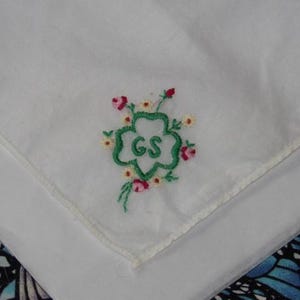 May include: White cotton handkerchief with green embroidered four-leaf clover with the letters "GS" in the center. The clover is surrounded by pink and white embroidered flowers.