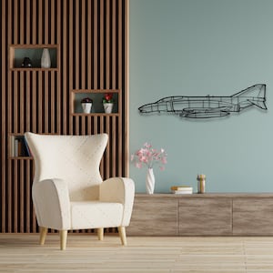 以下が含まれることがあります： 白い木製の脚が付いた白いアームチェアの真上に、薄い青色の壁に黒い金属製の戦闘機のアウトラインが飾られています。アームチェアは、棚が付いた木製の壁の前に置かれています。棚には植物が置かれています。