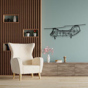 May include: A black metal wall art sculpture of a helicopter in a living room setting. The helicopter is hanging on a light blue wall above a white armchair and a wooden entertainment center.