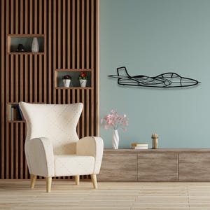 May include: A white armchair with a quilted design sits in front of a wooden wall with shelves. A black metal airplane silhouette is mounted on the wall above a wooden entertainment center.
