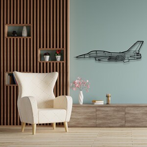 May include: A white armchair with a quilted pattern sits in a room with a wood slat wall and a black metal airplane silhouette on the wall. The room has a wooden entertainment center with a vase of pink flowers on top.
