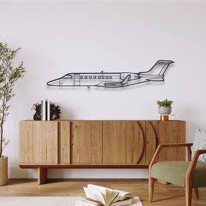 May include: A black metal wall art piece depicting a jet airplane. The artwork is mounted on a white wall above a wooden cabinet. The jet has detailed outlines of the windows, wings, and tail. The overall design is modern and minimalist.