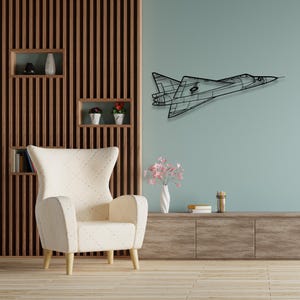 Può includere: Un'opera d'arte da parete in metallo nero raffigurante un aereo a reazione. L'opera è montata su una parete azzurra, con un mobile in legno e una poltrona color crema in primo piano. L'aereo è un contorno dettagliato.