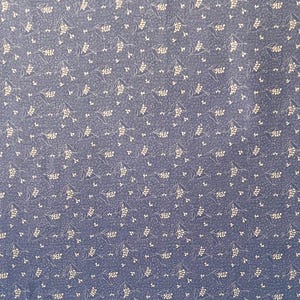 May include: A dark blue fabric featuring a repeating pattern of small, light-colored sprigs of leaves and tiny flowers. The textile has a consistent, dense print across the entire surface, creating a uniform appearance with a subtle, textured look.