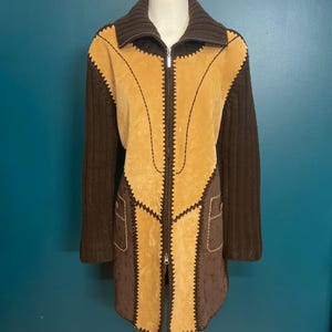 Peut inclure: Une veste en daim et en tricot marron et beige avec une fermeture éclair. La veste a un col montant et des manches longues.