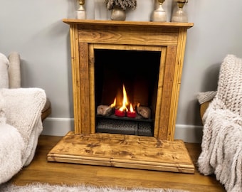 May include: A rustic wooden fireplace mantel with a black metal firebox and a glowing fire. The fireplace is decorated with red candles and has a wooden hearth.