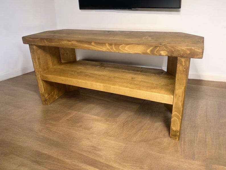 May include: A rustic wooden TV stand with a single shelf. The stand is made of natural wood with a warm brown finish. It has a simple, rectangular design with a slightly angled top.