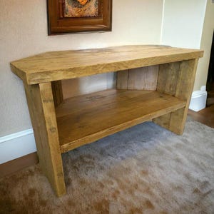 May include: A rustic wooden corner TV stand with a single shelf. The stand is made of reclaimed wood and has a natural finish.