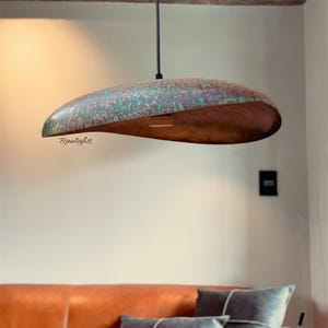 May include: A unique, handcrafted pendant light with a copper-colored interior and a textured, green-patina exterior. The light fixture is suspended from a black cord and features the text "Rumelights". This modern lighting fixture adds a touch of artistry to any space.