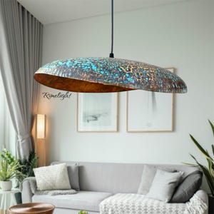 May include: A large, unique pendant light with a copper-colored interior and a textured, turquoise and brown exterior. The light fixture is suspended from a black cord and hangs above a gray sofa in a modern living room. The text "Rimelight" is visible on the light.