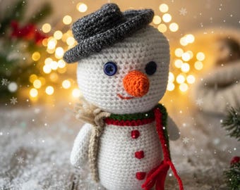 Peut inclure: Un bonhomme de neige crocheté à la main, avec un chapeau gris, des yeux en boutons bleus et un nez orange. Il porte une écharpe rouge et verte et une écharpe beige. Le bonhomme de neige est sur une surface en bois avec un effet neigeux et des lumières bokeh en arrière-plan.