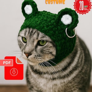 May include: A gray tabby cat wearing a green crochet frog costume with white accents. The image includes text that says "Balaclava Crochet PDF" and "Halloween Pets Costume". A red PDF icon is also visible.