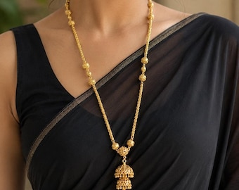 May include: A gold jewelry set consisting of a long necklace and matching jhumka earrings. The necklace features a delicate chain with small spherical beads and a tiered bell-shaped pendant. The earrings are matching bell-shaped jhumkas.