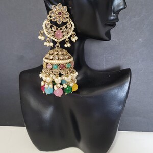 May include: An ornate gold-toned earring with a floral design and a pink gemstone. The earring features a bell-shaped bottom adorned with colorful beads in pink, green, blue, and yellow, and small white pearls.