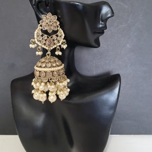 May include: Gold-toned chandelier earrings with a floral design and dangling faux pearls. The earrings are displayed on a black mannequin head against a gray background. The earrings have a detailed, ornate design.