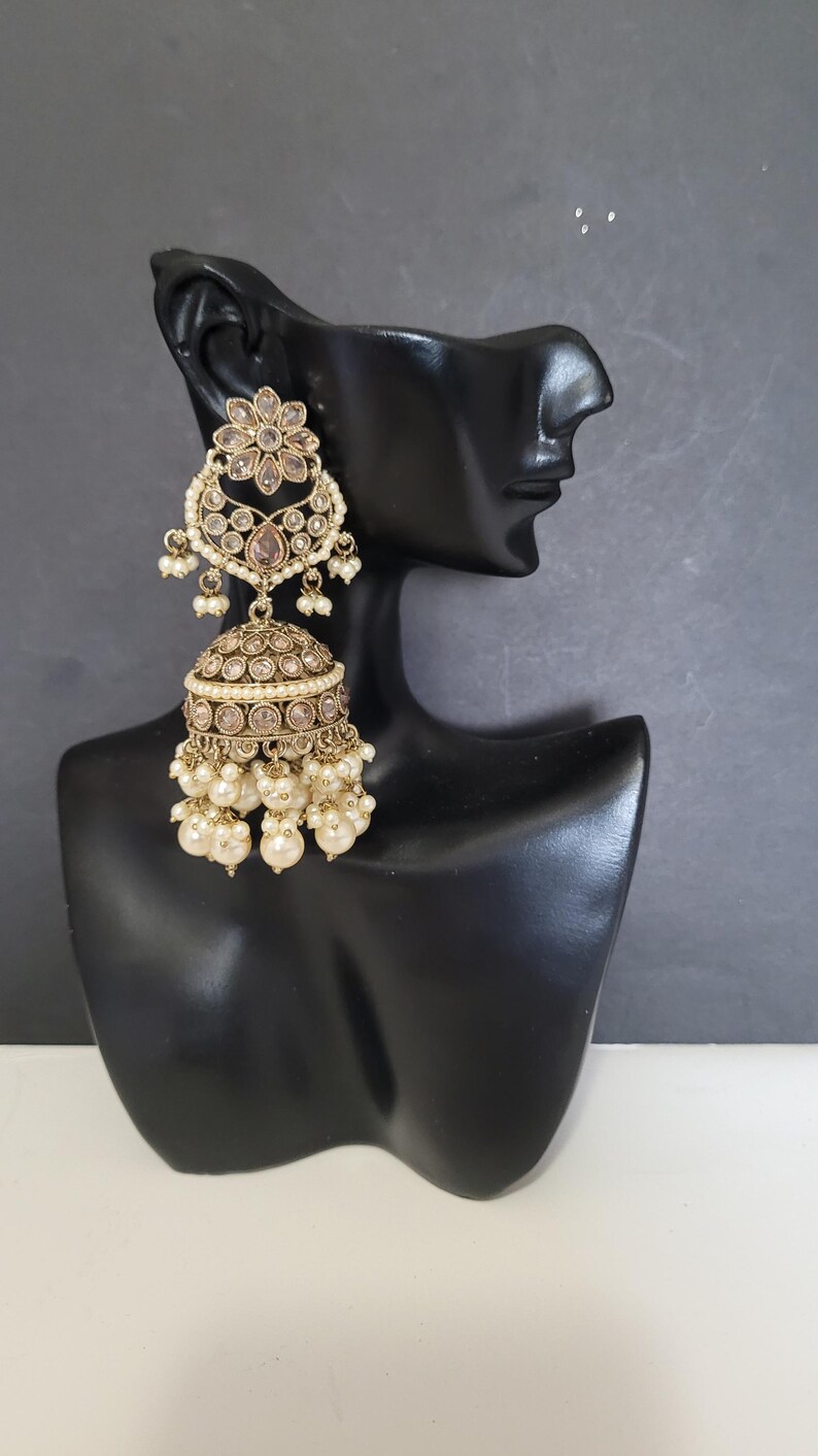 May include: Gold-toned chandelier earrings with a floral design and dangling faux pearls. The earrings are displayed on a black mannequin head against a gray background. The earrings have a detailed, ornate design.