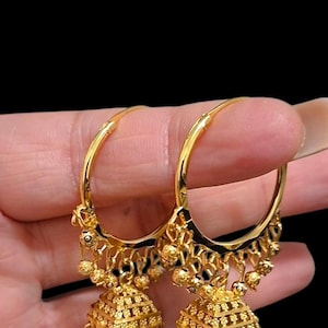 May include: A pair of gold hoop earrings with detailed patterns. The earrings have a bell-shaped design with small, round accents. They are held against a black background.