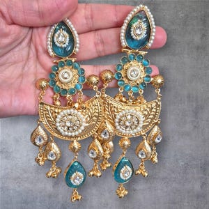 May include: A pair of ornate gold-toned earrings with intricate filigree and teardrop-shaped turquoise accents. The earrings feature a combination of pearls and clear gemstones, with a detailed floral design.
