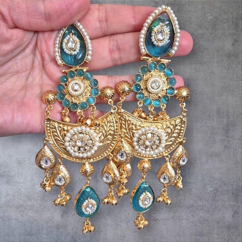 May include: A pair of ornate gold-toned earrings with intricate filigree and teardrop-shaped turquoise accents. The earrings feature a combination of pearls and clear gemstones, with a detailed floral design.