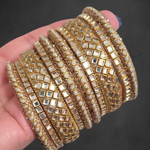 Peut inclure: Une pile de bracelets dorés avec un motif de miroirs et de perles. Les bracelets sont disposés en forme incurvée, la lumière se reflétant sur les surfaces miroitées. Ces bracelets sont un bijou traditionnel.