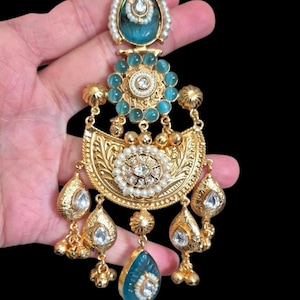 May include: Ornate gold-toned earring with turquoise and white accents. The earring features a teardrop-shaped turquoise stone at the bottom, with a floral design and dangling gold beads. The top has a turquoise stone surrounded by pearls.