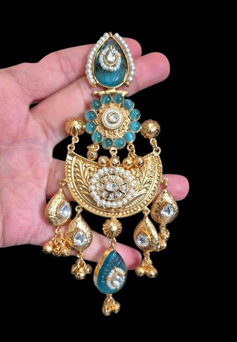 May include: Ornate gold-toned earring with turquoise and white accents. The earring features a teardrop-shaped turquoise stone at the bottom, with a floral design and dangling gold beads. The top has a turquoise stone surrounded by pearls.