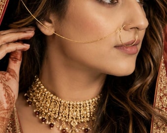 May include: A gold-toned choker necklace featuring intricate metalwork, small white pearls, and deep red beads. A matching gold nose ring is connected by a thin chain to a gold headpiece adorned with white pearls and red beads.