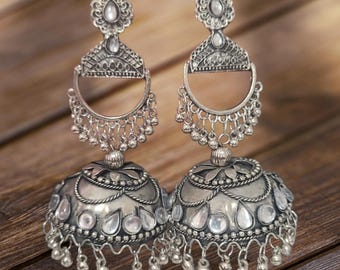 May include: A pair of silver-toned, ornate earrings. Each earring features a domed bell shape with clear stone accents and dangling beads. The design includes intricate filigree and a decorative top piece.